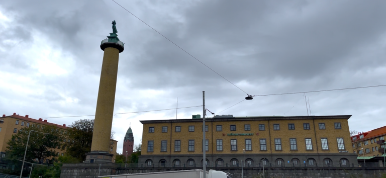 Gul byggnad med pelare och grön kupol under en molnig himmel.