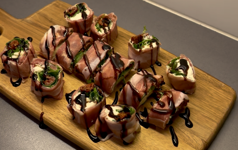 Italiensk Sushi (Prosciuttorullar) Förrätt med sushi bitar på ett skärbräda, dekorerad med sås och grönsaker.