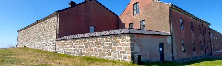 Fästning med gamla byggnader och en grön gräsyta i förgrunden.