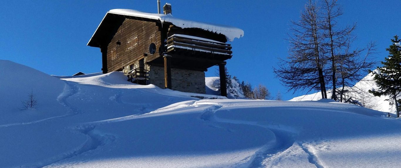 La Thuile - Italien En stuga på snötäckta backar under en klarblå himmel. Spår syns i snön.