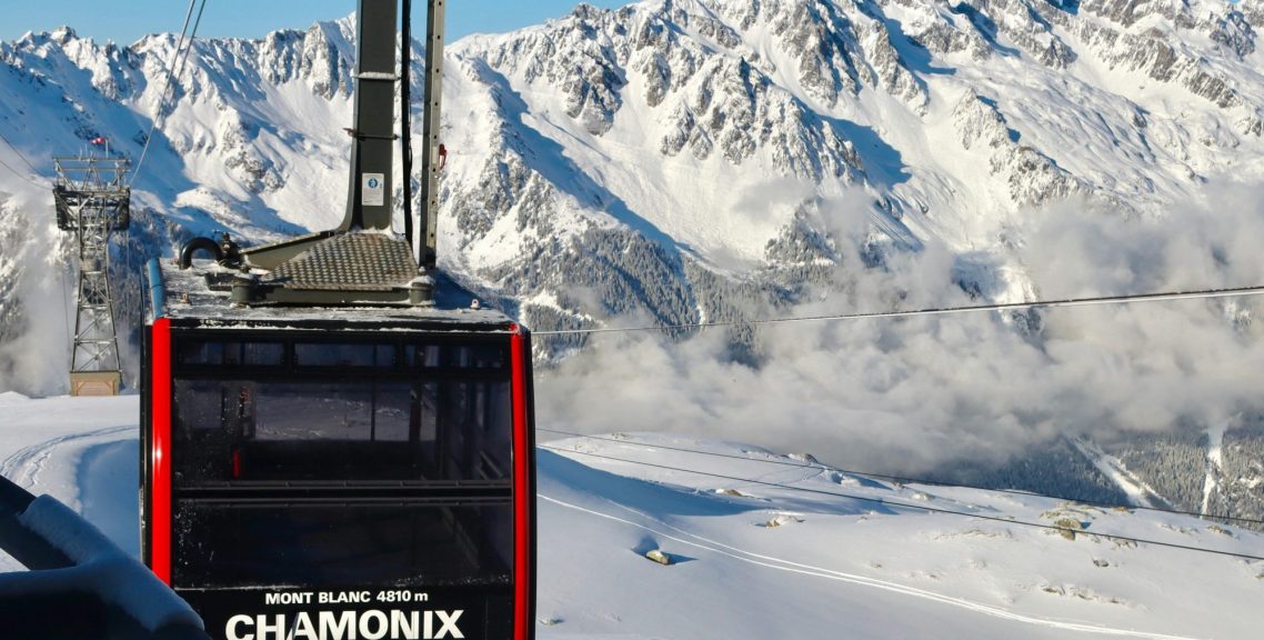Gondolåkning i Chamonix med snötäckta berg och moln i bakgrunden.