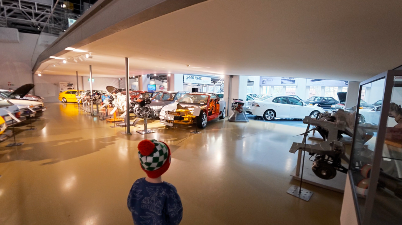 Bilsalongen Saab Car Museum En person i mössa står i en bilutställning med flera bilar och ljus.
